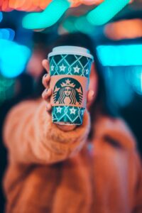 starbucks brand positoning - woman on brown jacket showing green and brown Starbucks coffee cup